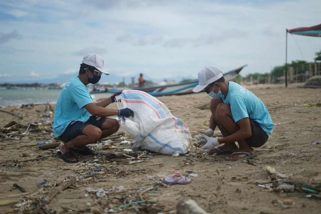 Two Indonesian men clean up lastics on the beach on behalf of an ocean cleanup group.